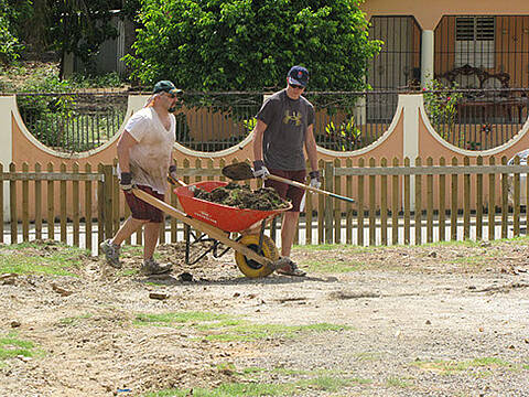 Two male volunteers cleaning up with a red wheel barrow