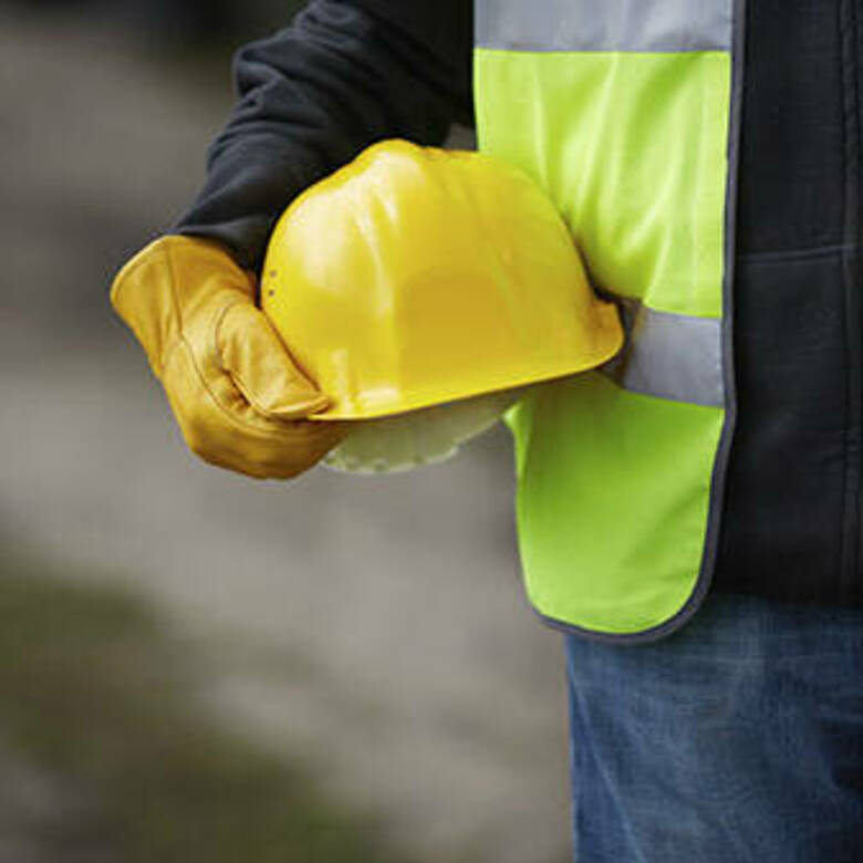 construction worker holding a yellow hard-hat at their side