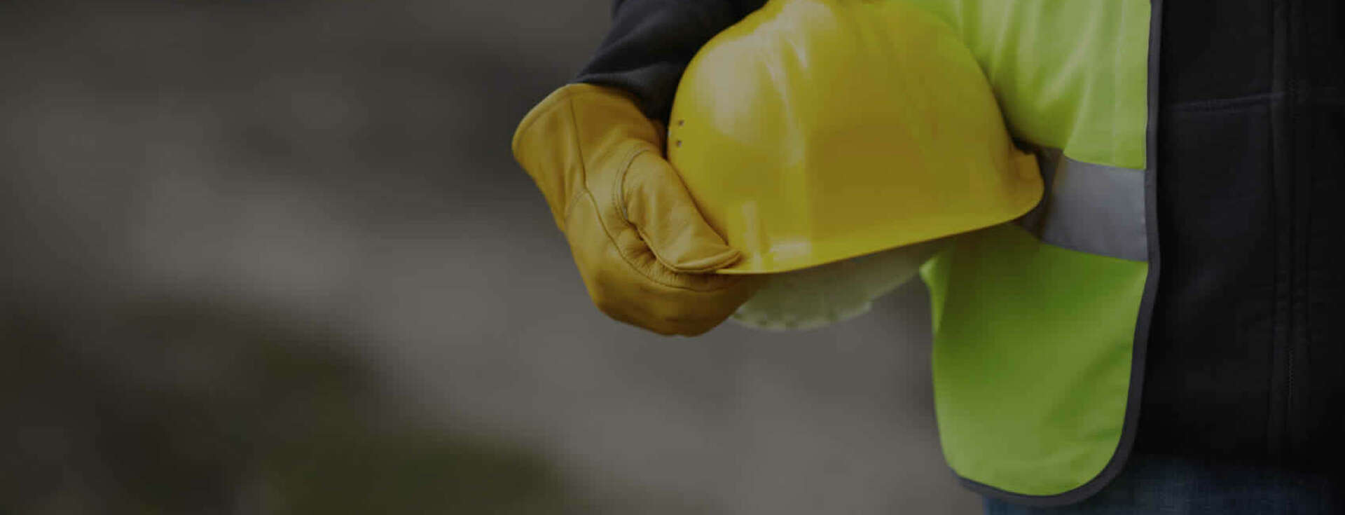 construction worker holding a yellow hard-hat at their side.